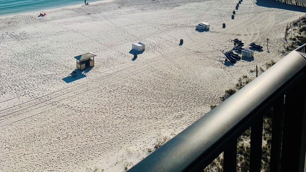 A beach with a wooden pier extending into the water, a lifeguard tower, and several beach umbrellas. - Beachfront condo with amazing views of the sunset, family friendly, and safe. (Panama City Beach)
