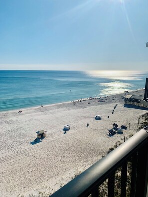 A beach with a wooden pier extending into the water, a lifeguard tower, and several beach umbrellas. - Beachfront condo with amazing views of the sunset, family friendly, and safe. (Panama City Beach)