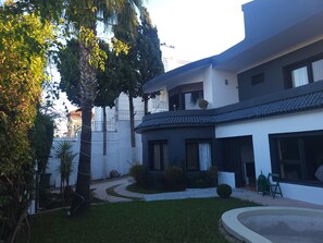 Une maison moderne à deux étages, dotée d’un toit incurvé, d’un petit jardin et d’une façade blanche.