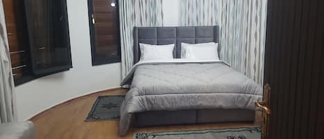 Une chambre à coucher avec un lit, deux fenêtres, une porte et une chaise.