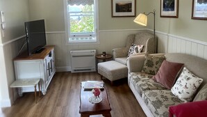 A living room with a television, a window with a view of greenery, a lamp, and a sofa with floral cushions. - Gorgeous cottage in the heart of the picturesque Huon Valley. (Castle Forbes Bay)