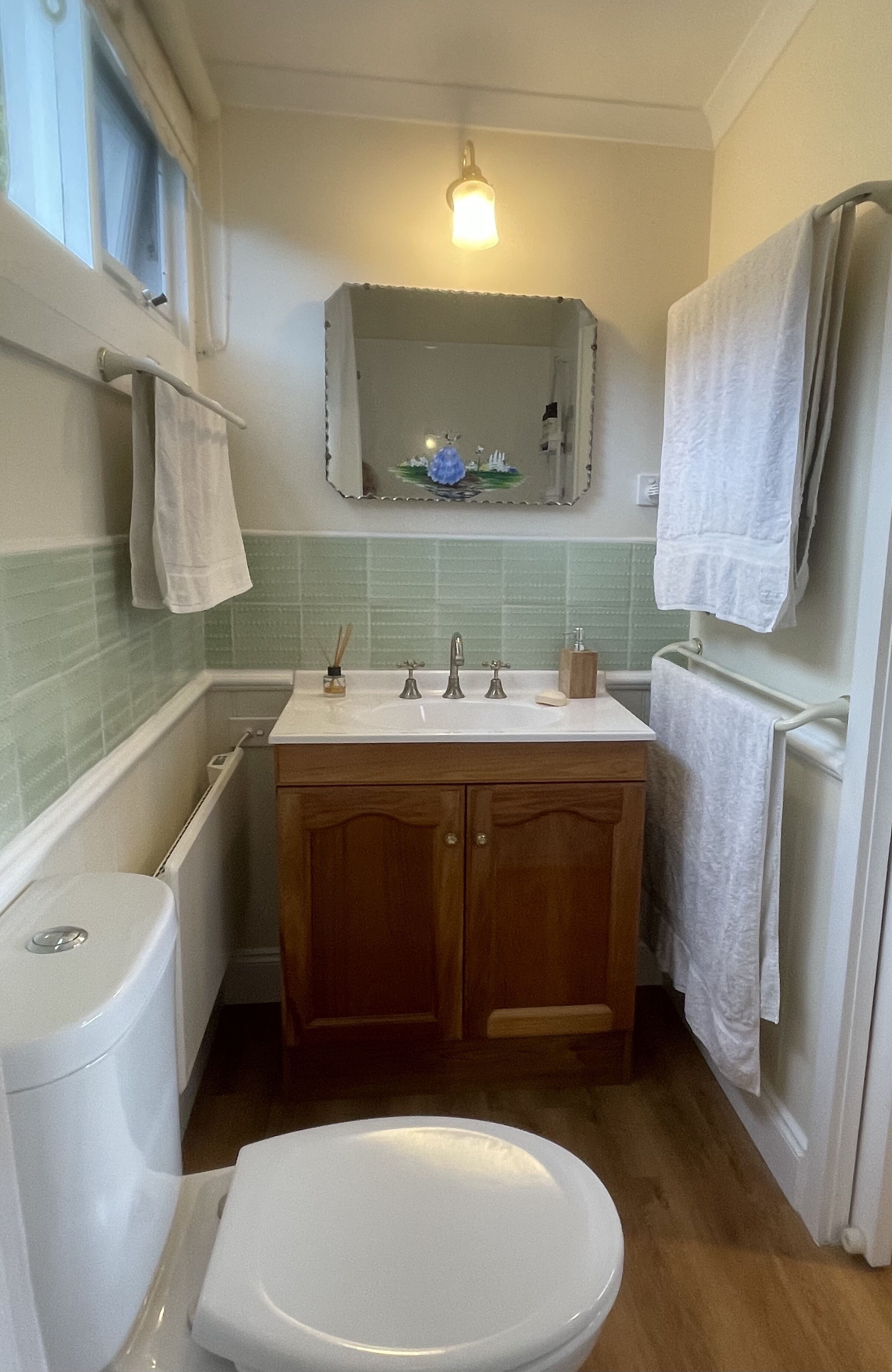 Une petite salle de bain avec des toilettes blanches, un lavabo surmonté d’un miroir et des meubles en bois.
