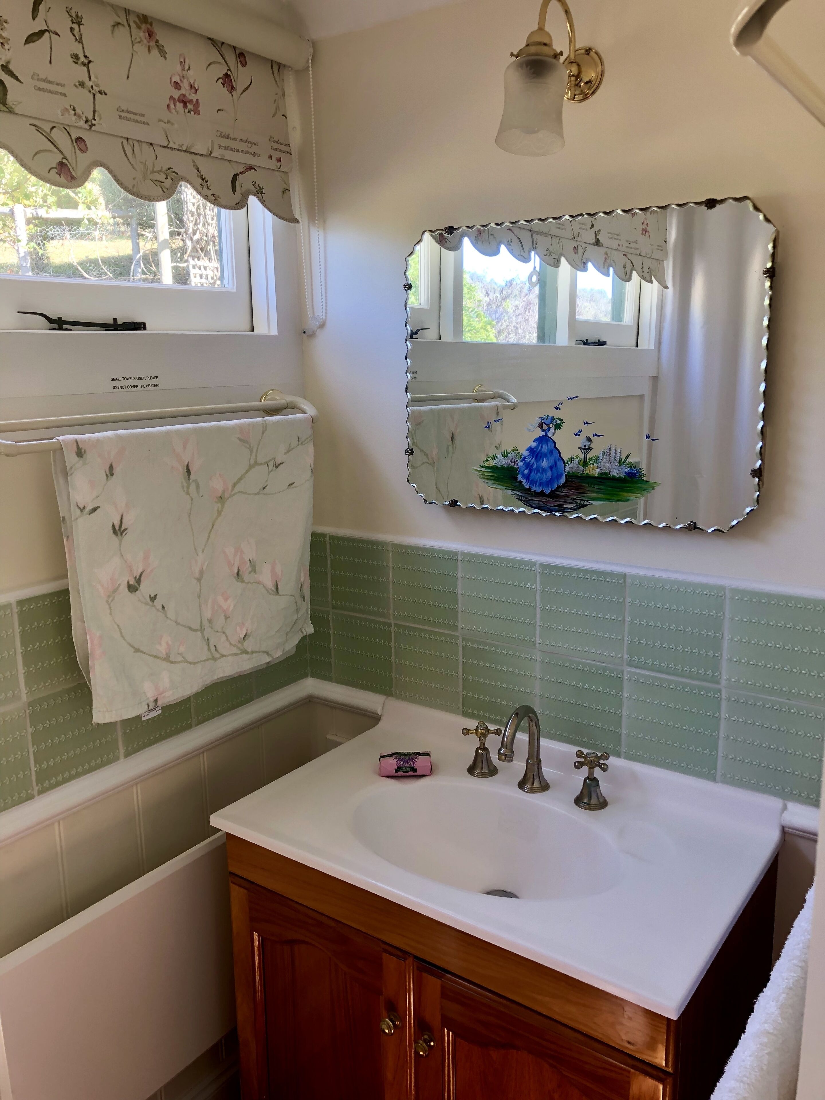 A bathroom with a white sink, a mirror with a floral frame, a towel rack, and a green tiled wall.