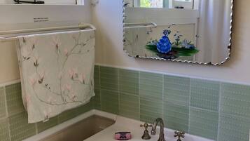 A bathroom with a white sink, a mirror with a floral frame, a towel rack, and a green tiled wall.