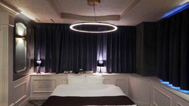 A hotel room with a large bed, a round ceiling light, a mirror, and dark curtains.