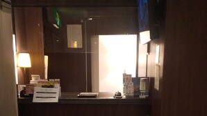 A small reception area with a desk, a chair, a lamp, and a window.