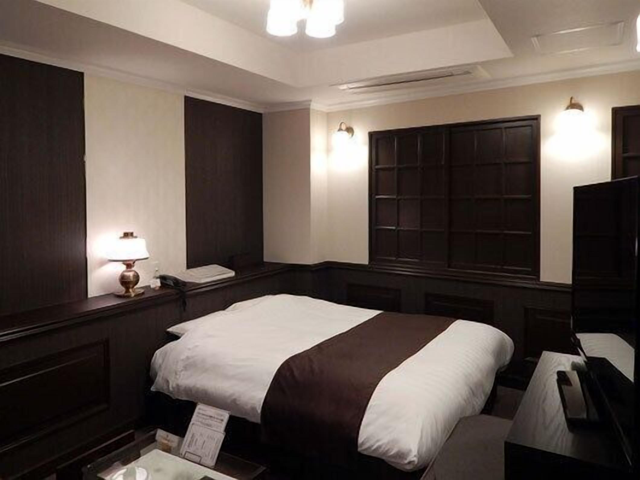 A hotel room with a bed, a nightstand, a lamp, a mirror, and a window with a view.