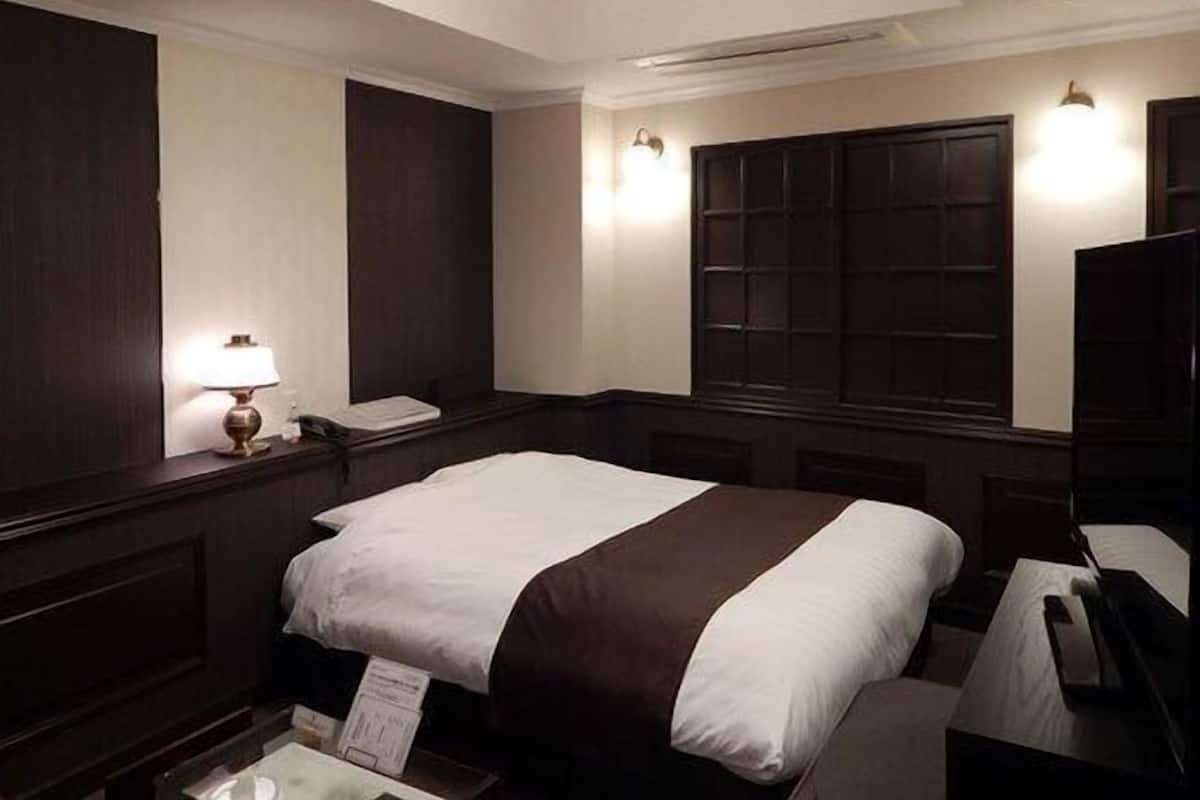 Une chambre d’hôtel avec un lit, une table de chevet, une lampe, un miroir et une fenêtre donnant sur un paysage agréable.