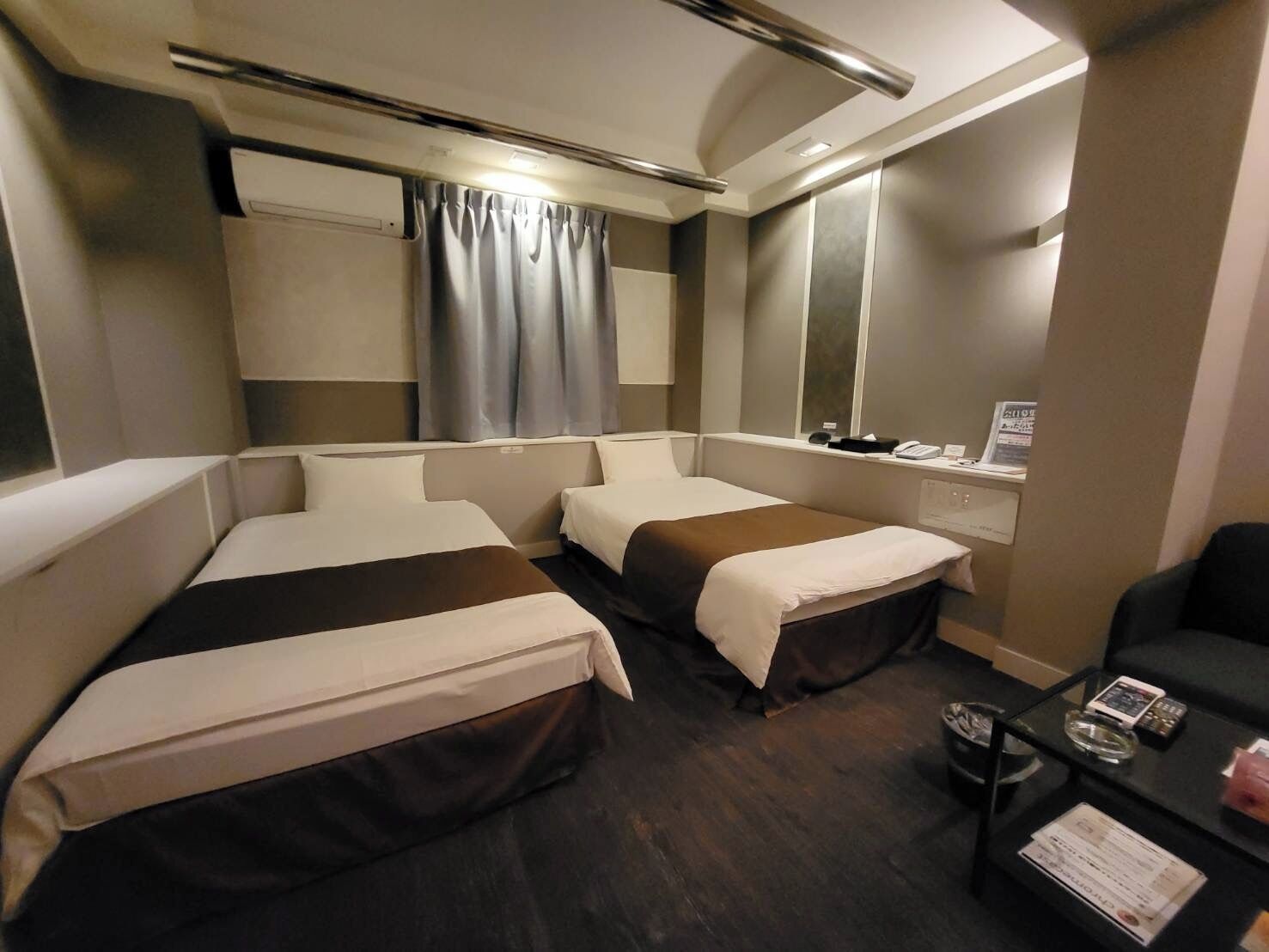 A hotel room with two beds, a desk with a chair, a mirror, and a window with curtains.