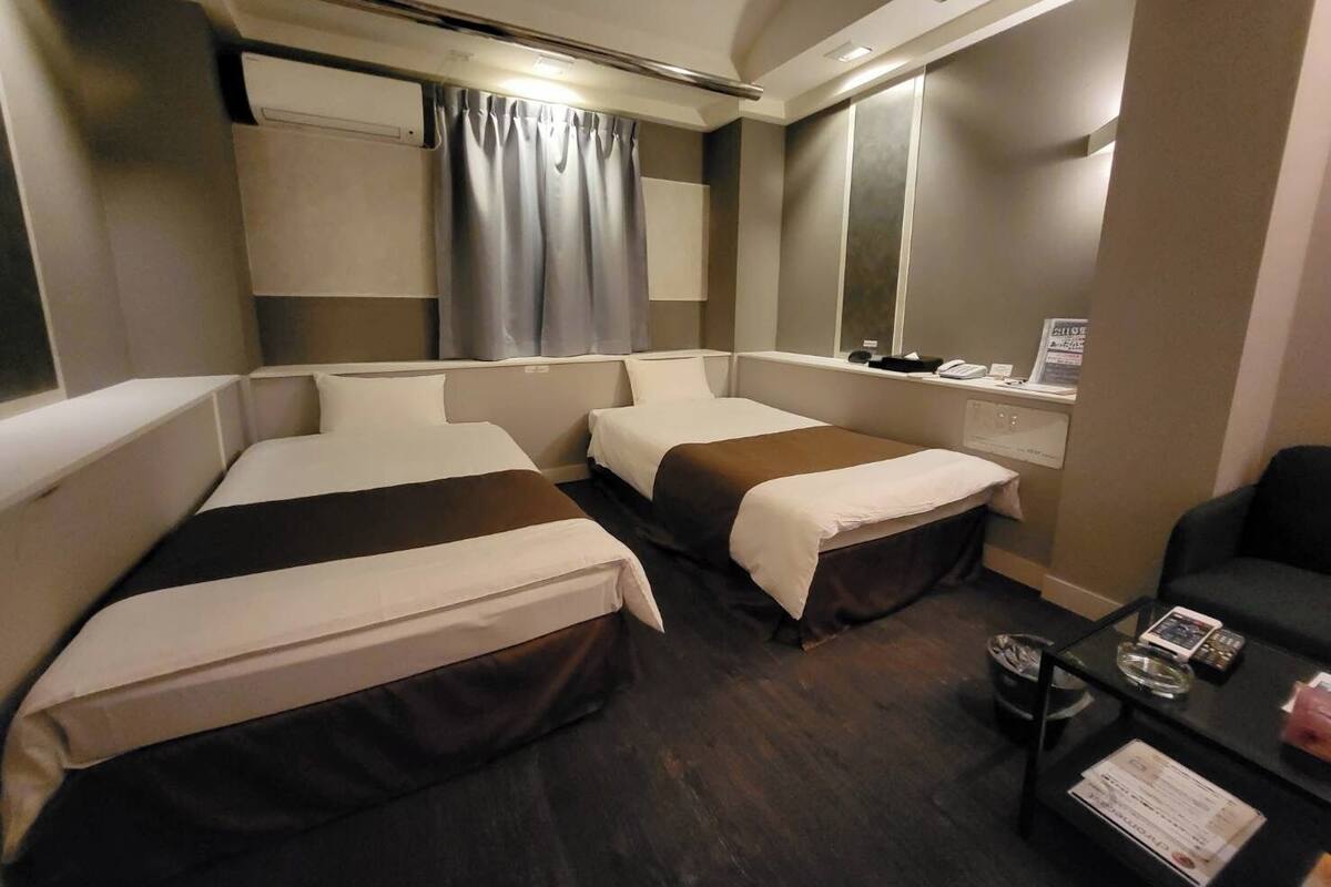 Une chambre d’hôtel avec deux lits, un bureau avec une chaise, un miroir et une fenêtre avec des rideaux.