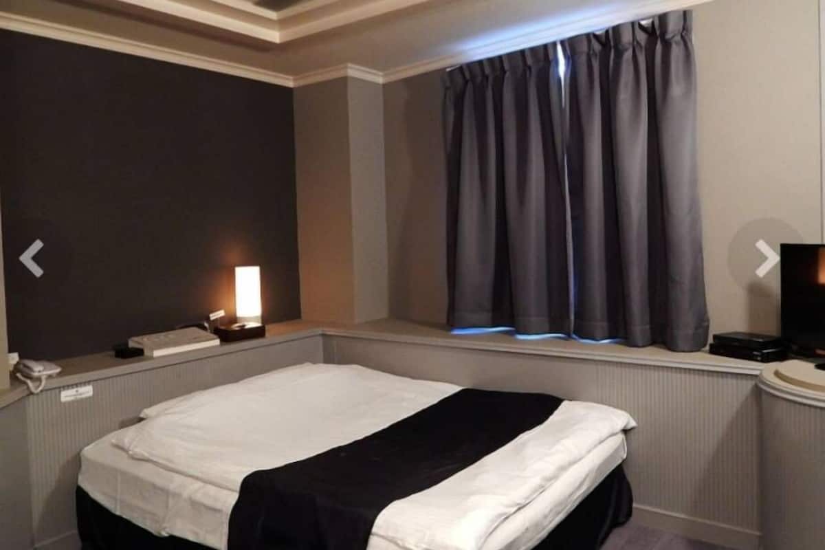 Une chambre d’hôtel comprenant un lit, une table de chevet avec une lampe, une fenêtre avec des rideaux et un téléviseur.