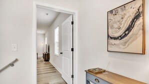 A hallway with a wooden floor, white walls, a door, and a framed abstract painting. - Pet-Friendly 2BR Greer Home, King Beds & Fire Pit (Greer)