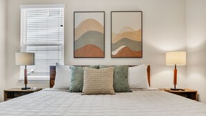A neatly made bed with a quilted cover, two wall-mounted artworks depicting abstract landscapes, and bedside lamps on wooden nightstands. - Family & Pets Welcome: 2BR in DT Greer w/ Fire Pit (Greer)