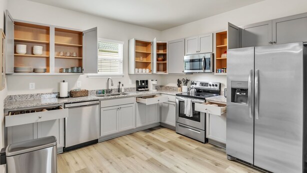 A modern kitchen with white cabinets, stainless steel appliances, and wooden shelves. - Family & Pets Welcome: 2BR in DT Greer w/ Fire Pit (Greer)