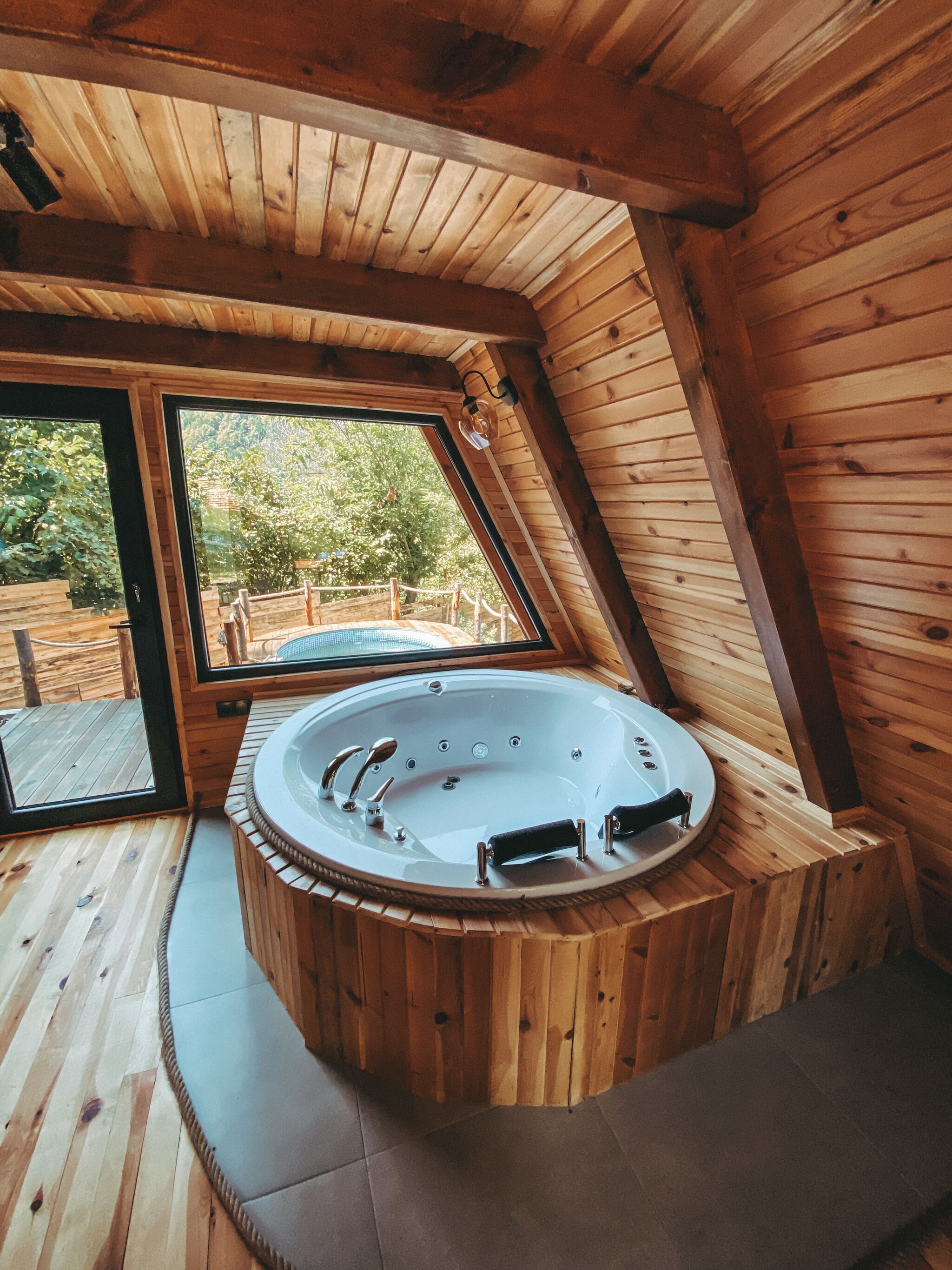 Een houten hut met een jacuzzi, grote ramen en een houten terras.