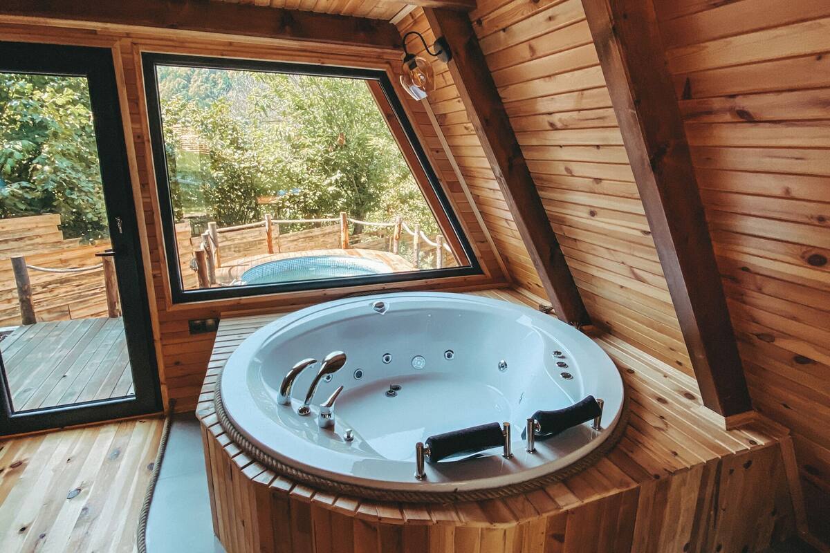 A wooden cabin with a hot tub, large windows, and a wooden deck.