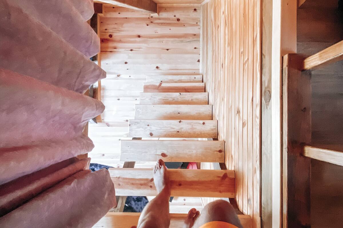 A wooden staircase with a person sitting on it, wooden walls, and a window.