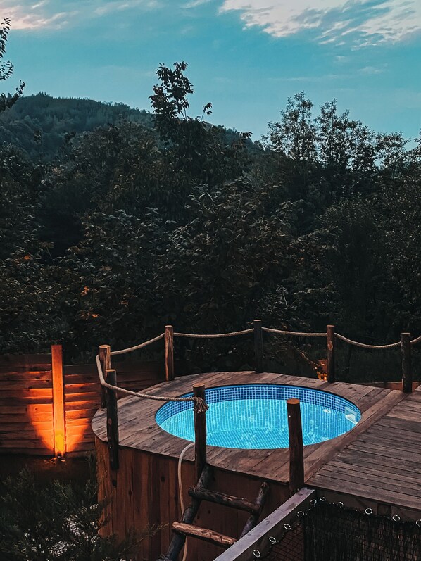 A wooden deck with a pool, surrounded by a rope fence, overlooking a forested area.