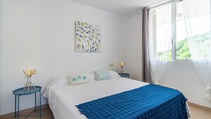 Une chambre à coucher avec un lit, une table de chevet, une lampe fixée au mur et une fenêtre avec des rideaux.