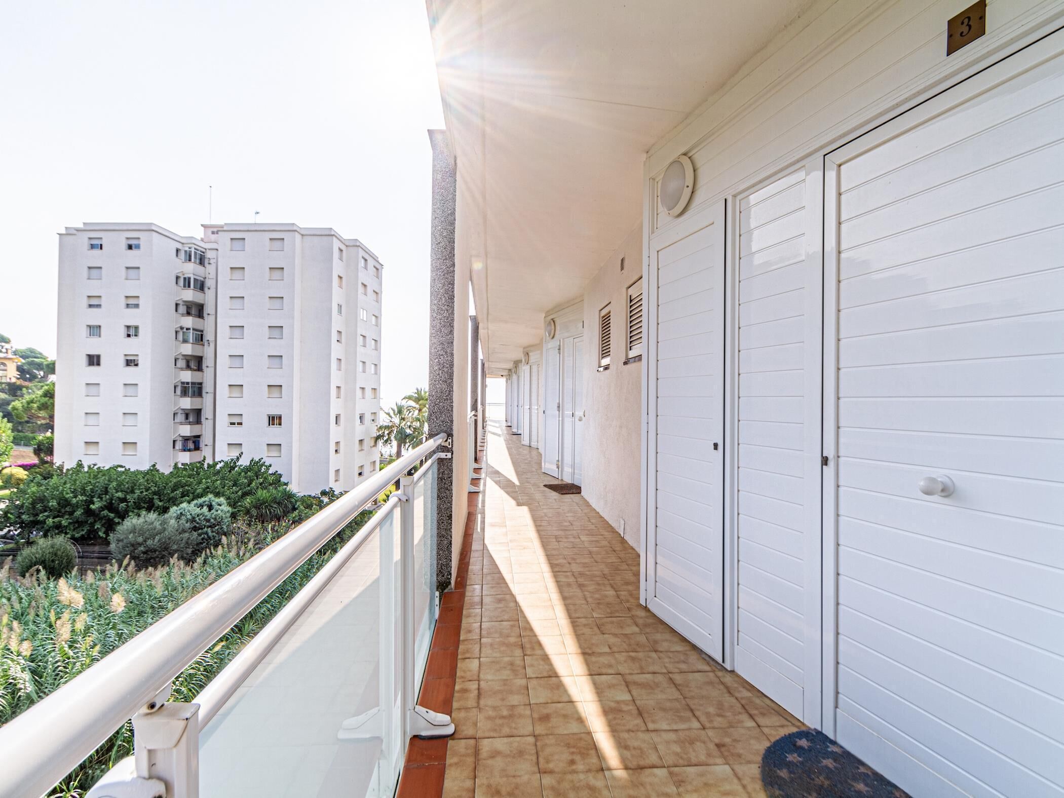 Ein Balkon mit weißer Brüstung, gefliestem Boden und einer Reihe weißer Garagentore.