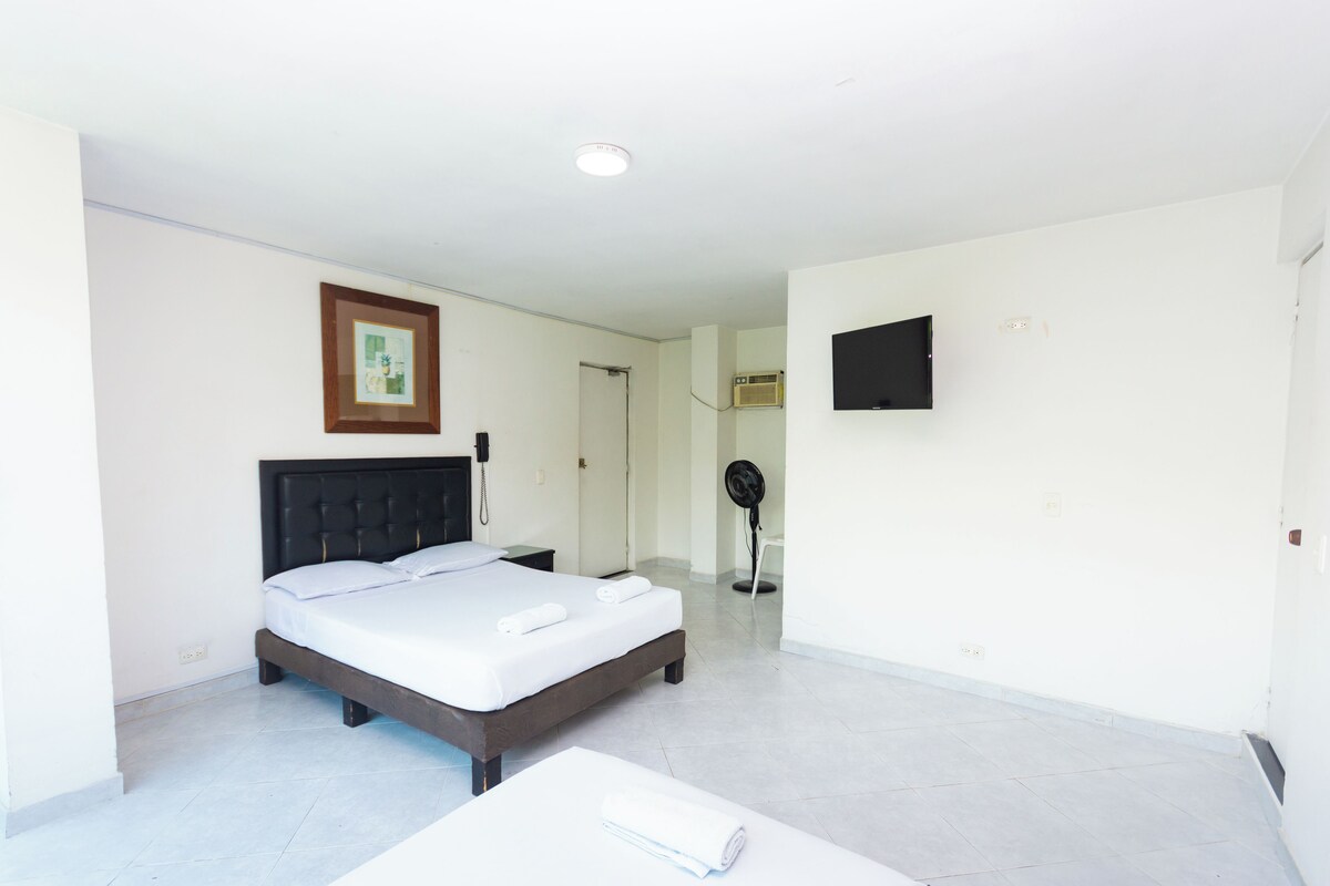 Habitación de hotel con cama, mesita de noche, televisor montado en la pared y ventilador de techo.