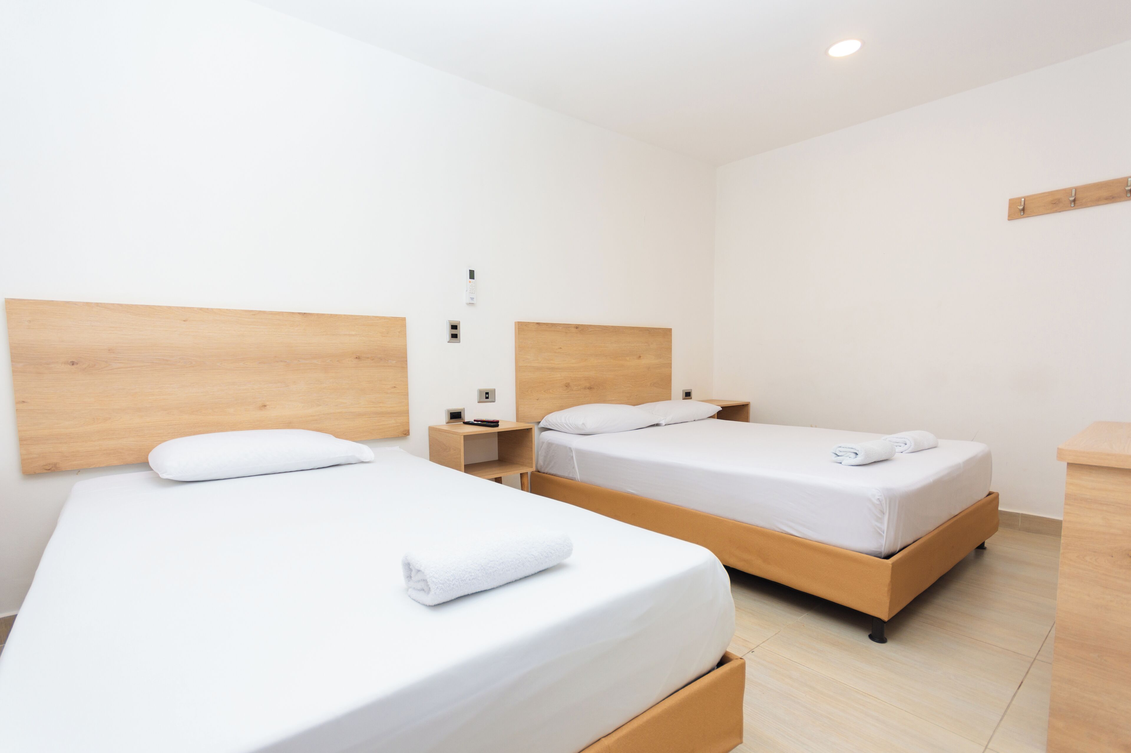 Una habitación de hotel con dos camas individuales, cabeceros de madera, ropa de cama blanca, una mesita de noche pequeña con una lámpara y una mesita auxiliar de madera.