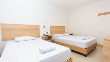 Una habitación de hotel con dos camas individuales, cabeceros de madera, ropa de cama blanca, una mesita de noche pequeña con una lámpara y una mesita auxiliar de madera.