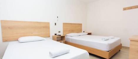Una habitación de hotel con dos camas individuales, cabeceros de madera, ropa de cama blanca, una mesita de noche pequeña con una lámpara y una mesita auxiliar de madera.