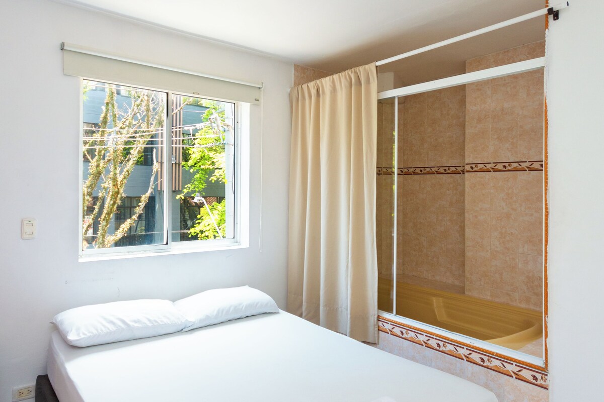 A bedroom with a bed, a window, and a shower area.