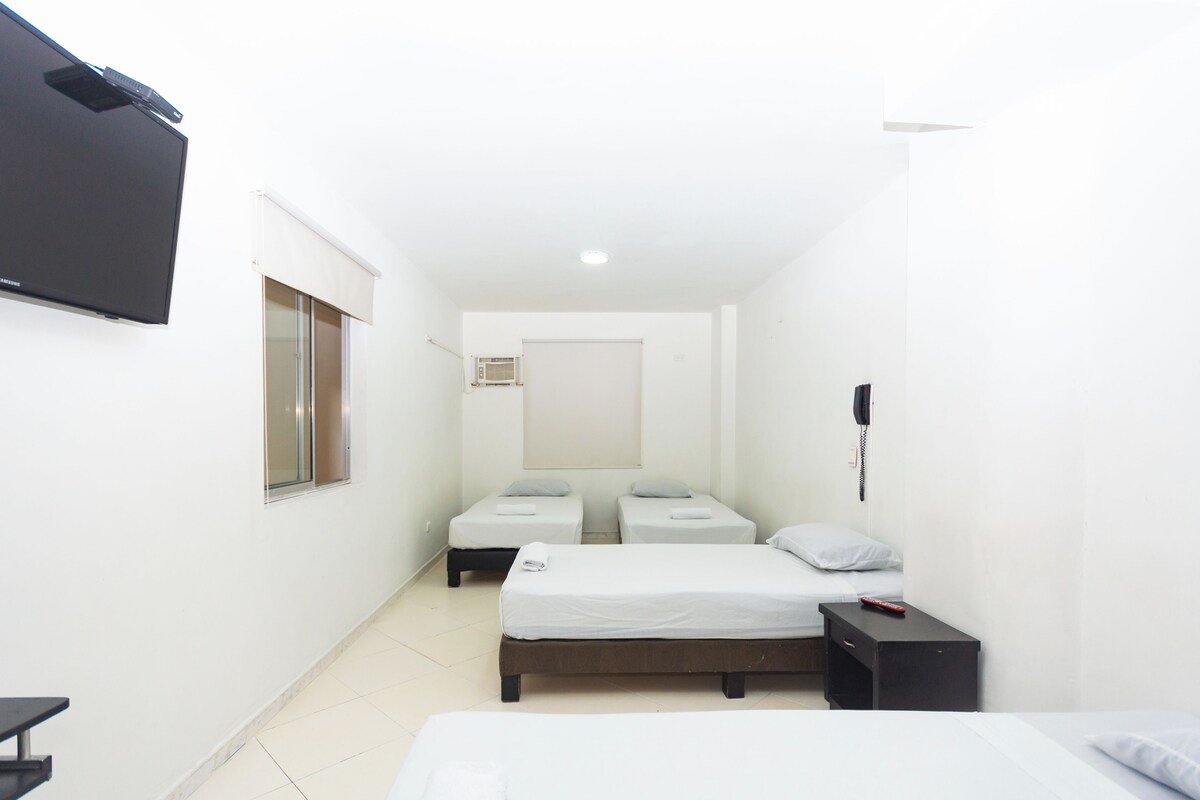 A small, clean room with two single beds, a desk, a chair, and a TV mounted on the wall.