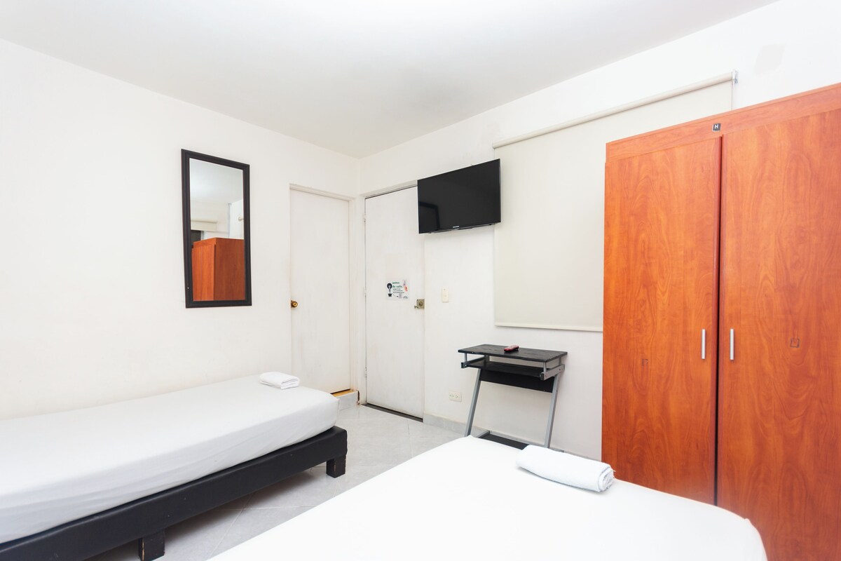 Una habitación con una cama individual, un armario de madera, un televisor montado en la pared y un escritorio pequeño con una silla.