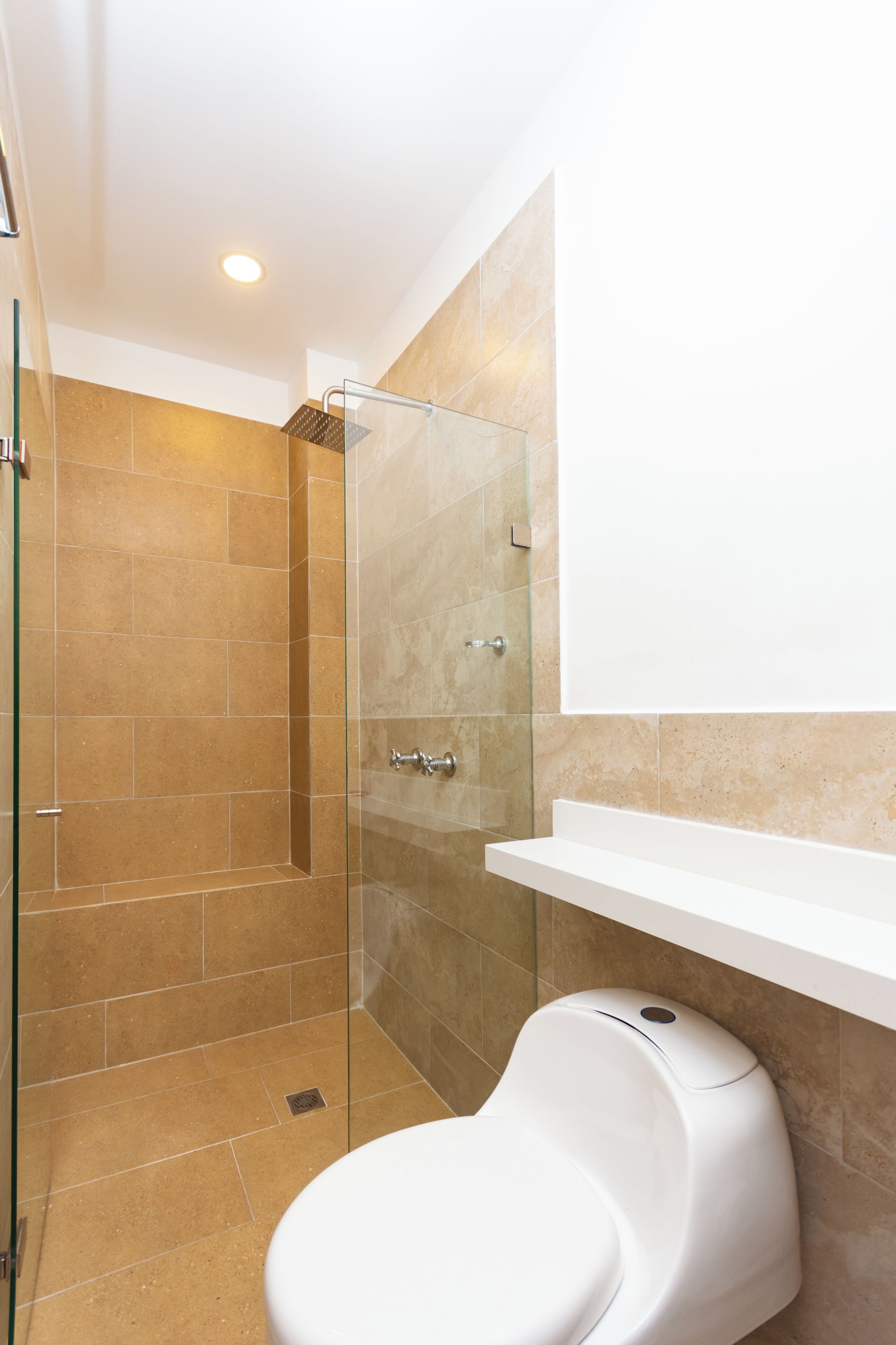 A modern bathroom with a glass-enclosed shower, a white toilet, and a beige tiled wall.