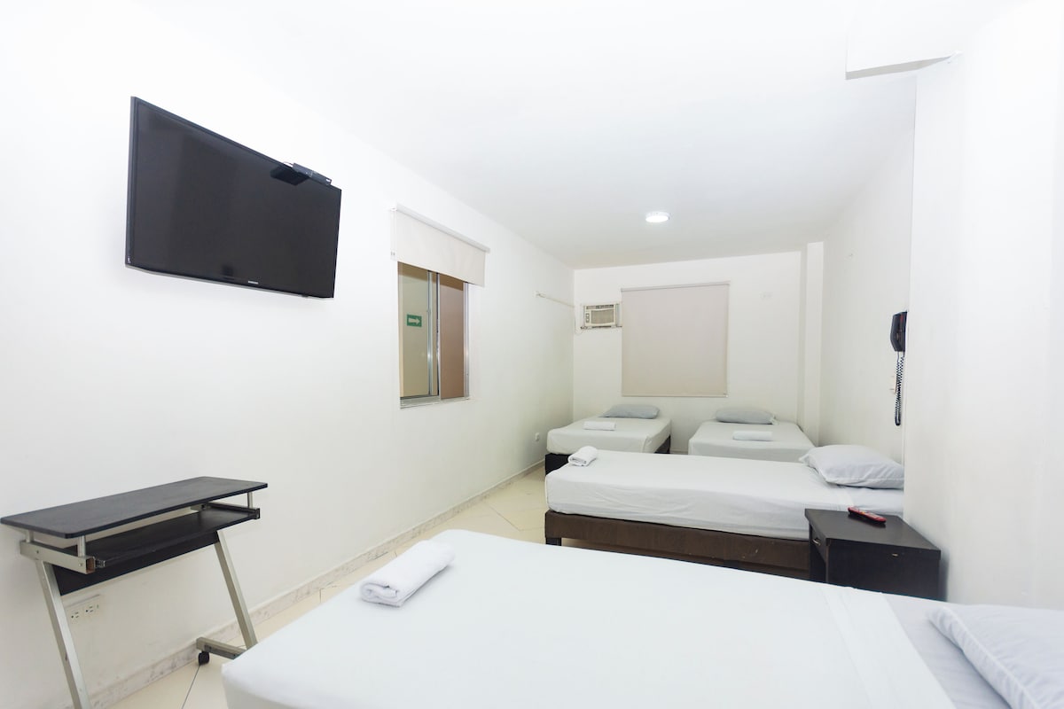 Habitación de hotel con cama, escritorio, televisor montado en la pared y una ventana pequeña.