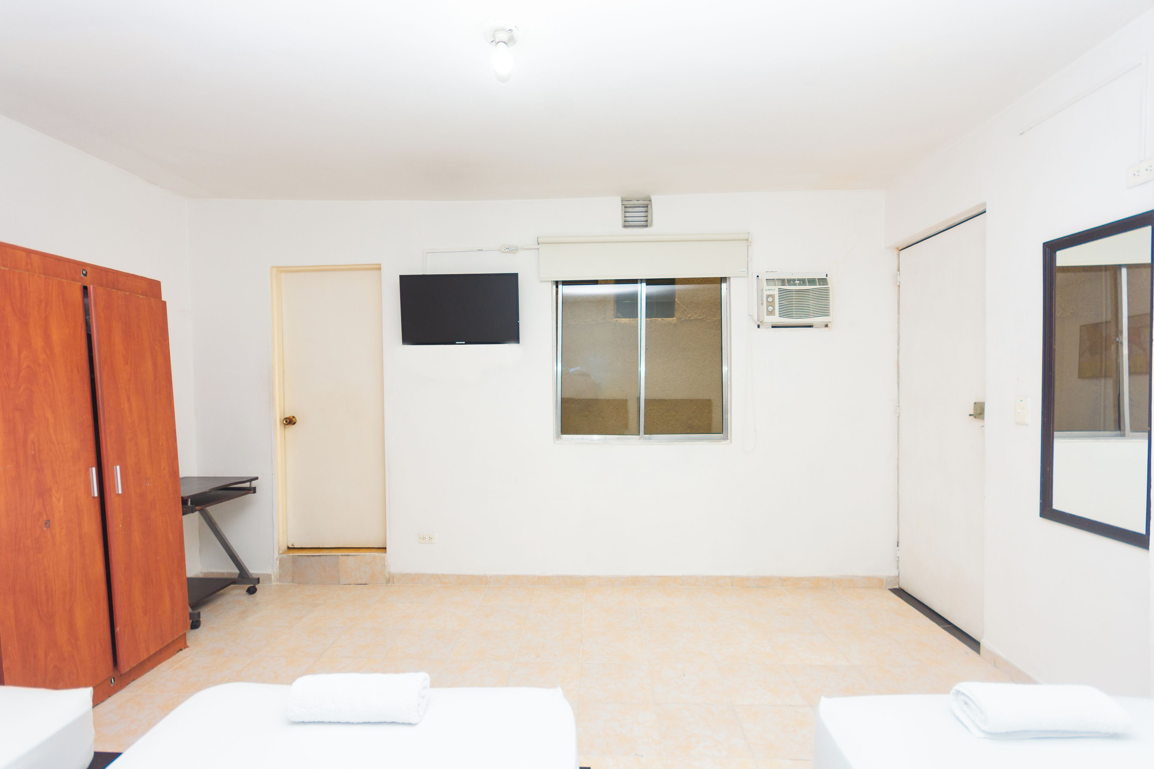 Habitación de hotel con cama, escritorio, armario, televisor, ventana y puerta al baño.