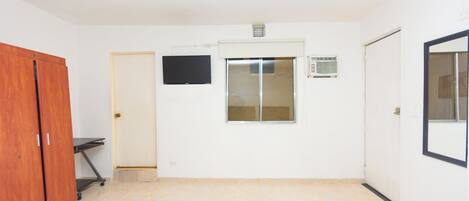 Habitación de hotel con cama, escritorio, armario, televisor, ventana y puerta al baño.
