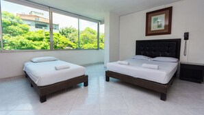A hotel room with two beds, a large window with a view of greenery, a framed picture on the wall, and a bedside telephone. - Hotel Villa Real (Medellín)