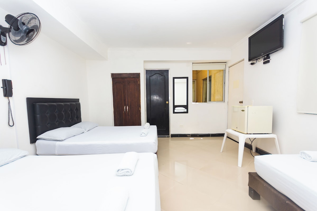 Habitación de hotel con dos camas, un televisor, un espejo y una puerta que da a un baño.