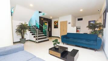 Una sala de estar moderna con un sofá azul, una mesa de centro con una planta, una escalera y un mueble de madera.