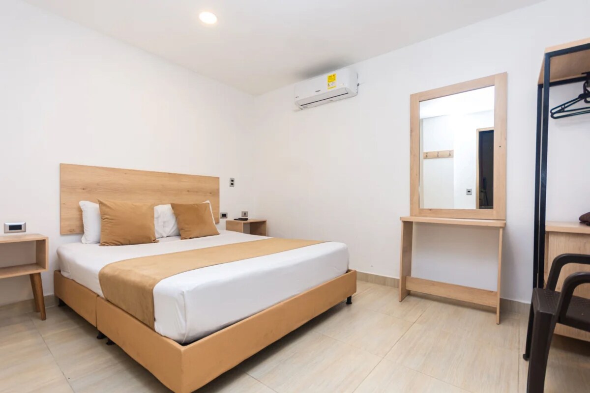 A hotel room with a bed, bedside tables, a mirror, and a wardrobe.