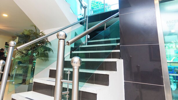 A modern staircase with glass railings and metal handrails, leading to an upper floor. - Hotel Villa Real (Medellín)