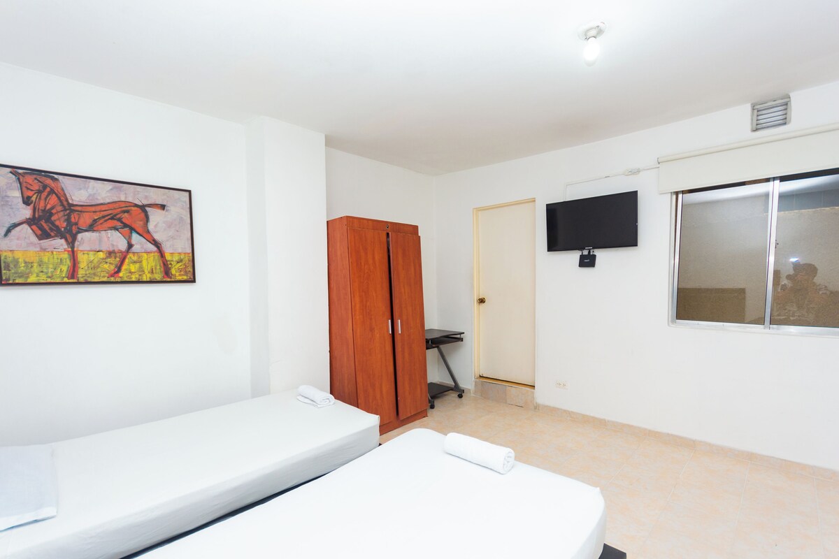 Habitación de hotel con cama, armario de madera, televisor montado en la pared y un cuadro.