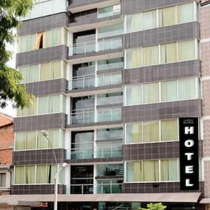Un edificio de hotel de varios pisos con diseño moderno, que cuenta con grandes ventanales y un llamativo letrero con la palabra 'HOTEL' en la fachada.