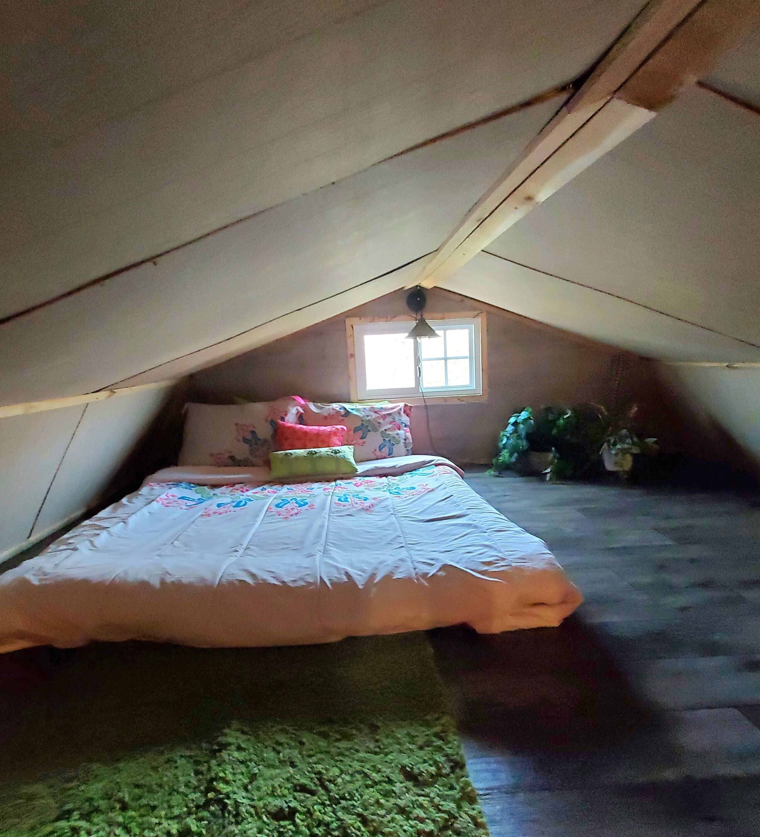 Ein kleines Schlafzimmer im Dachgeschoss mit einem Einzelbett, einem Fenster und einem Deckenventilator.