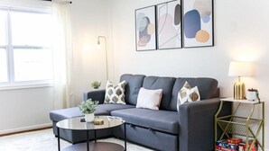 Ein modernes Wohnzimmer mit einem grauen Sofa, einem runden Couchtisch und abstrakten Wandbildern.