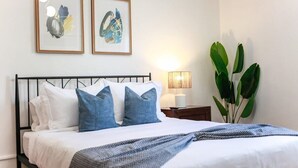 Ein ordentlich bezogenes Bett mit weißer und blauer Bettwäsche, einem schwarzen Metallkopfteil und zwei gerahmten abstrakten Bildern an der Wand.