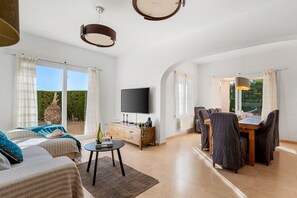 A spacious living area with a flat-screen TV, a dining table with chairs, and a large window offering a view of the outdoors. - Villa Gran Sol 13 - PlusHolidays (Calpe)