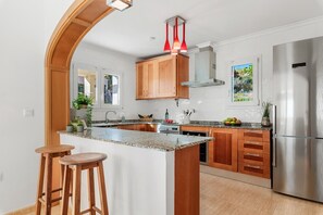 A modern kitchen with wooden cabinets, a granite countertop, and a stainless steel refrigerator. - Villa Gran Sol 13 - PlusHolidays (Calpe)