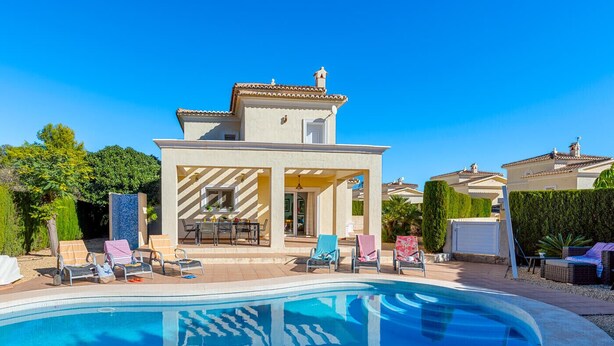 A poolside area with a clear blue pool, lounge chairs, and a building with a tiled roof. - Villa Gran Sol 13 - PlusHolidays (Calpe)