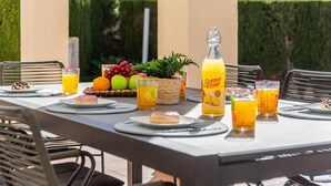 An outdoor dining area with a table set for a meal, including plates, glasses, and a bottle of juice. - Villa Gran Sol 13 - PlusHolidays (Calpe)