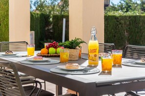 An outdoor dining area with a table set for a meal, including plates, glasses, and a bottle of juice.